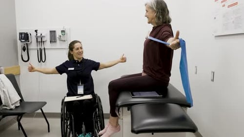 Physical therapist in wheelchair guides patient with resistance band in medical clinic