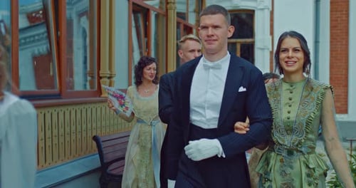 Beautiful Women in Ball Gowns with Fans in Their Hands Walk Arm in Arm with Men in Tailcoats and