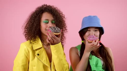 Two Stylish Friends Enjoy Eating Sweet Donuts