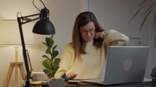 Woman with neck pain working at desk in home office