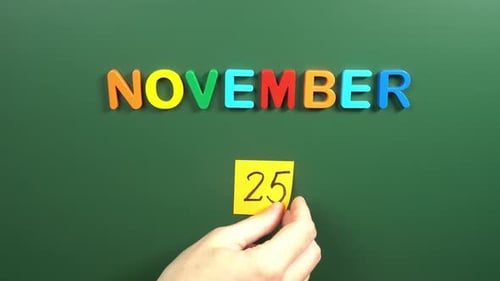 Hand sticking a sticker 25 November calendar day on school board. 25 date of November. Twenty fifth