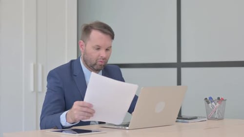 Businessman Celebrating Success at Office Desk With Laptop