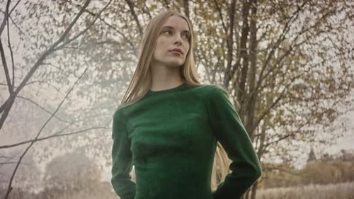 Model gracefully posing outdoors in a flowing green dress within a tranquil forest setting
