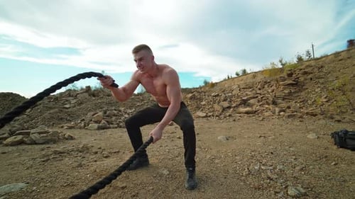 Atleta haciendo entrenamiento con cuerdas de combate Hombre joven musculoso haciendo ejercicio con cuerdas de combate