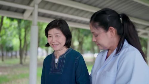 The smiling face of an elderly Asian woman taking a walk outside and the nurse supporting