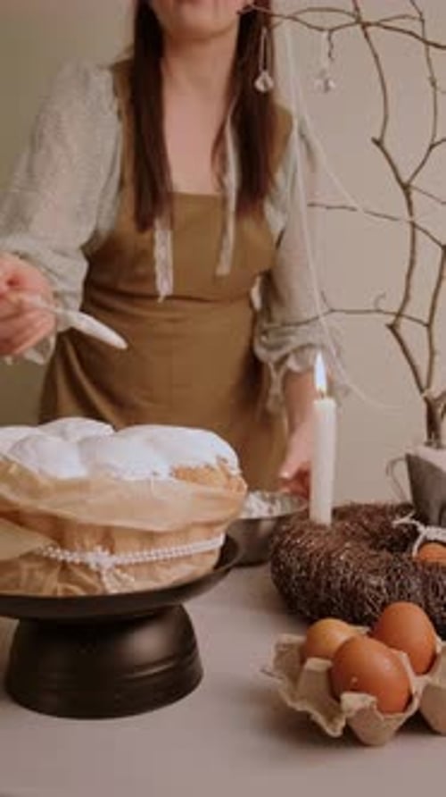 Young woman in cozy clothes spreading white icing on an Easter cake enjoying the process of holiday