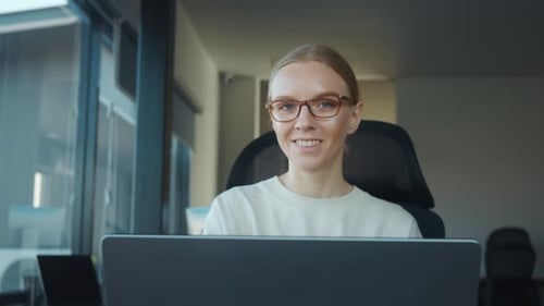 Die junge Assistentin der Geschäftsleitung mit Brille arbeitet fleißig an ihrem Laptop in Bright Modern
