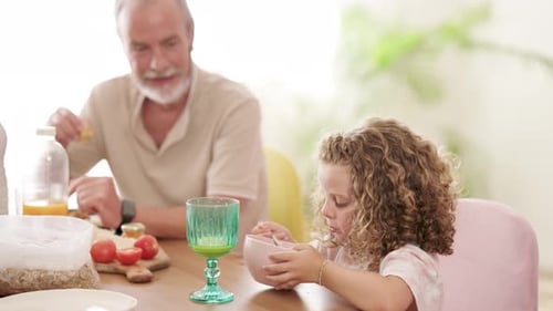Grandfather and Granddaughter Eating Breakfast at Table Indoors