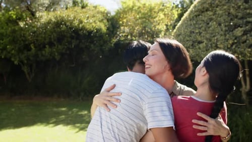 Family hugging and smiling together in garden, enjoying outdoor time