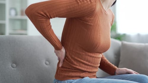 Close up. Female hand holding massaging lower back. Tired young adult woman suffering from back pain