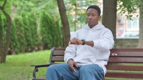 Young Adult on Bench Checking Smartwatch in Park