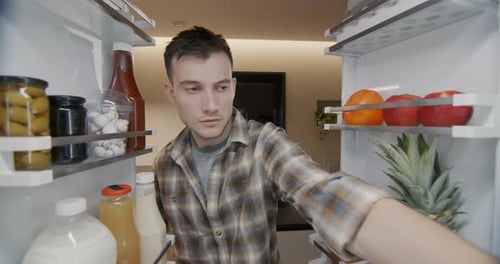 A Young Man Takes a Container with Breakfast From the Refrigerator View From Inside the Refrigerator