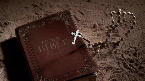 Crucifix Rosary Bead Necklace Falling Onto Bible and Dusty Surface.