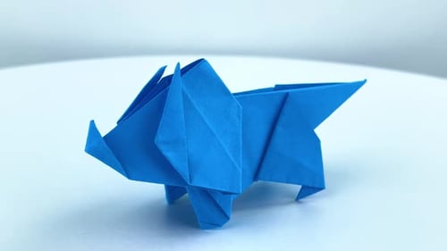 Origami de dinosaurio girando sobre una superficie blanca
