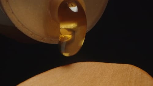 I pour honey from a bottle onto a wooden spoon. Dolly slider extreme close-up.