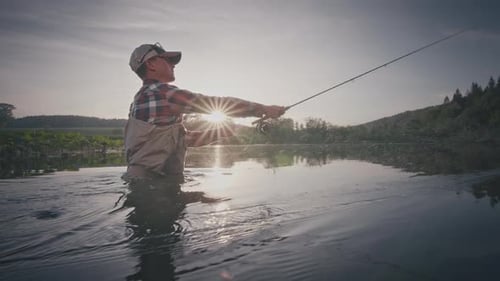 Fly fishing. Angler stands in the river and casts the fly at sunset