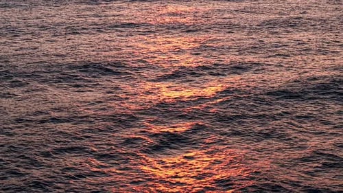 Golden sunlight reflects on gentle ocean waves at sunset, creating a serene and warm atmosphere