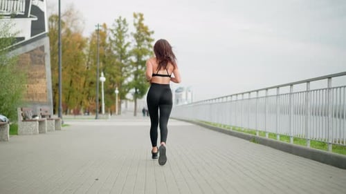 Woman Jogging in Black Athletic Wear in Park with Benches and Iron Fence