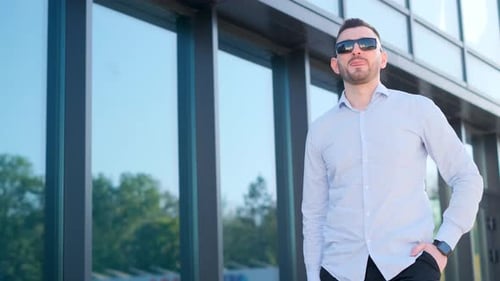A Young Man Stands Near an Office Building and Looks at His Watch in Bright Sunlight Stylish Look of