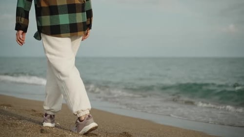 A young woman in white pants walks along the sea on the sand, slow motion.