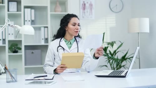 Happy smiling female doctor in white coat received letter with great news sitting in office at workp