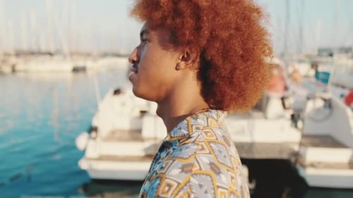 Side view of young happy man walking against the backdrop of white yachts in summer and smiling