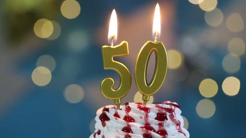 50th birthday. Blowing out number shaped candles on cupcake against blurred background with lights