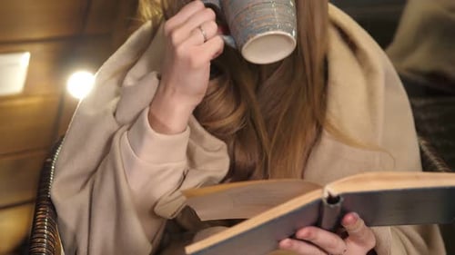 Woman Reading Book and Drinking Warm Beverage Indoors