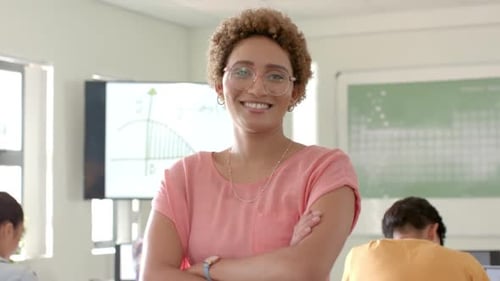 Smiling teacher standing in classroom with students studying in background at high school