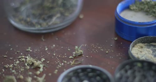 Marijuana grinders filled with weed and kief on a wood background. Pan right.