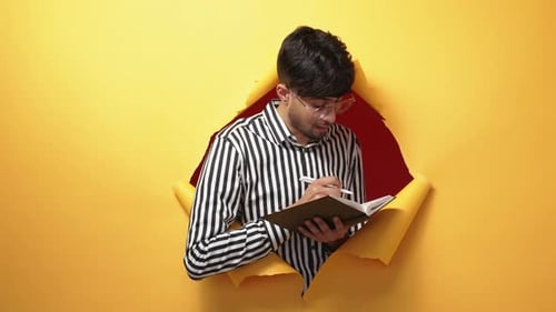 Young Adult Writes in Notebook Through Torn Paper