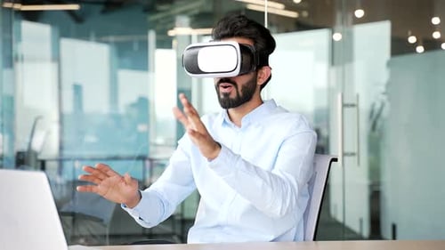 Young bearded businessman works using VR glasses in virtual reality simulator while sitting