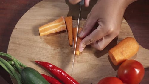 Frische Karotten mit einem Messer auf einem Holzschneidebrett in lange Stücke schneiden