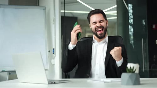 Successful Businessman Celebrating with Phone in Modern Office