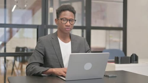 Afroamerikaner zeigt auf die Kamera, während er am Laptop arbeitet