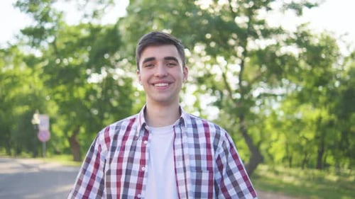 In an Outdoor Portrait a Young Man in a Plaid Shirt is Smiling Amid Sunny and Serene Surroundings