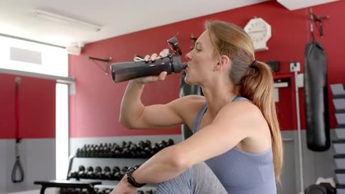 Fit young Caucasian woman takes a water break at the gym
