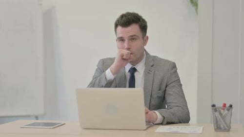 Man in Suit Coughing at Desk with Laptop