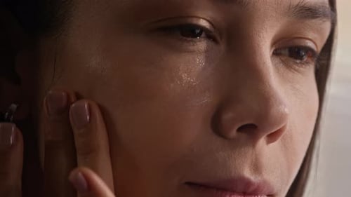 Woman Applies Cream to Face in Close Up