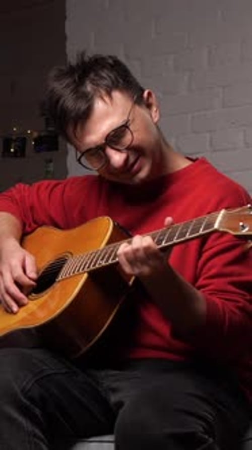 Man plays acoustic guitar sitting on a couch