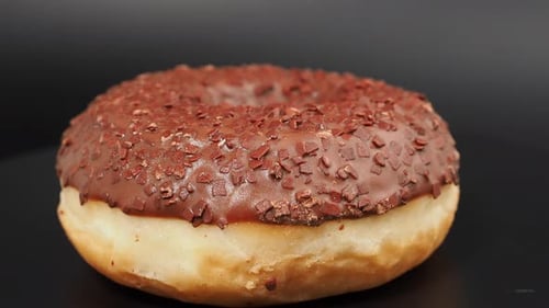 Rotating chocolate donut with chocolate chips on a black background.