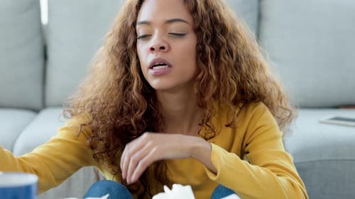 Sick young woman with flu or an allergy sneezing in a tissue and blowing nose