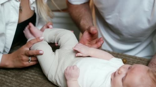 Unrecognized Caucasian parents stand near the baby lying on the plaid.