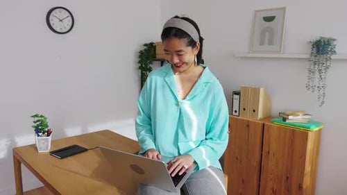 Smiling Asian Woman Working on Laptop in Minimalist Home Office