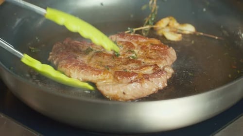 Close Up Professional Chef Turns Over with Tongs Piece of Meat Frying on a Pan