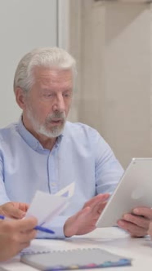 Senior Man Discusses Tablet With Colleague at Office