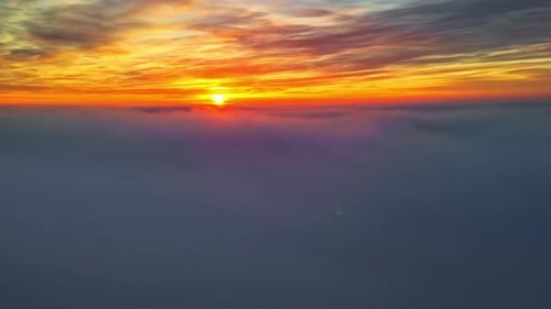 Shot of sunset above fluffy layers of clouds scattering vibrant orange and red color hues in sky.