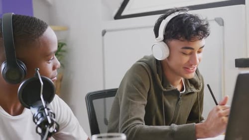 Amis adolescents masculins heureux et diversifiés utilisant un ordinateur portable et enregistrant un podcast, Ralenti