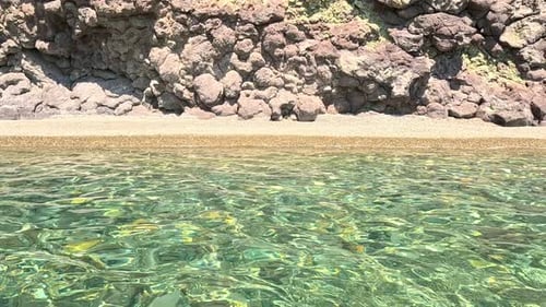 Sea Water Surface Camera Flies Over the Calm Azure Sea with Volcanic Rocky Shores on Background