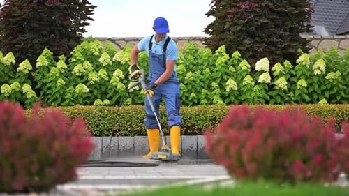 Caucasian Garden Worker Pressure Washing Residential Driveway Using Modern Pressure Washer